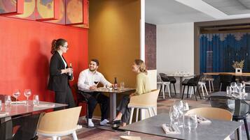 A modern restaurant with a vibrant red wall, a large mural, and a mix of black and white chairs.