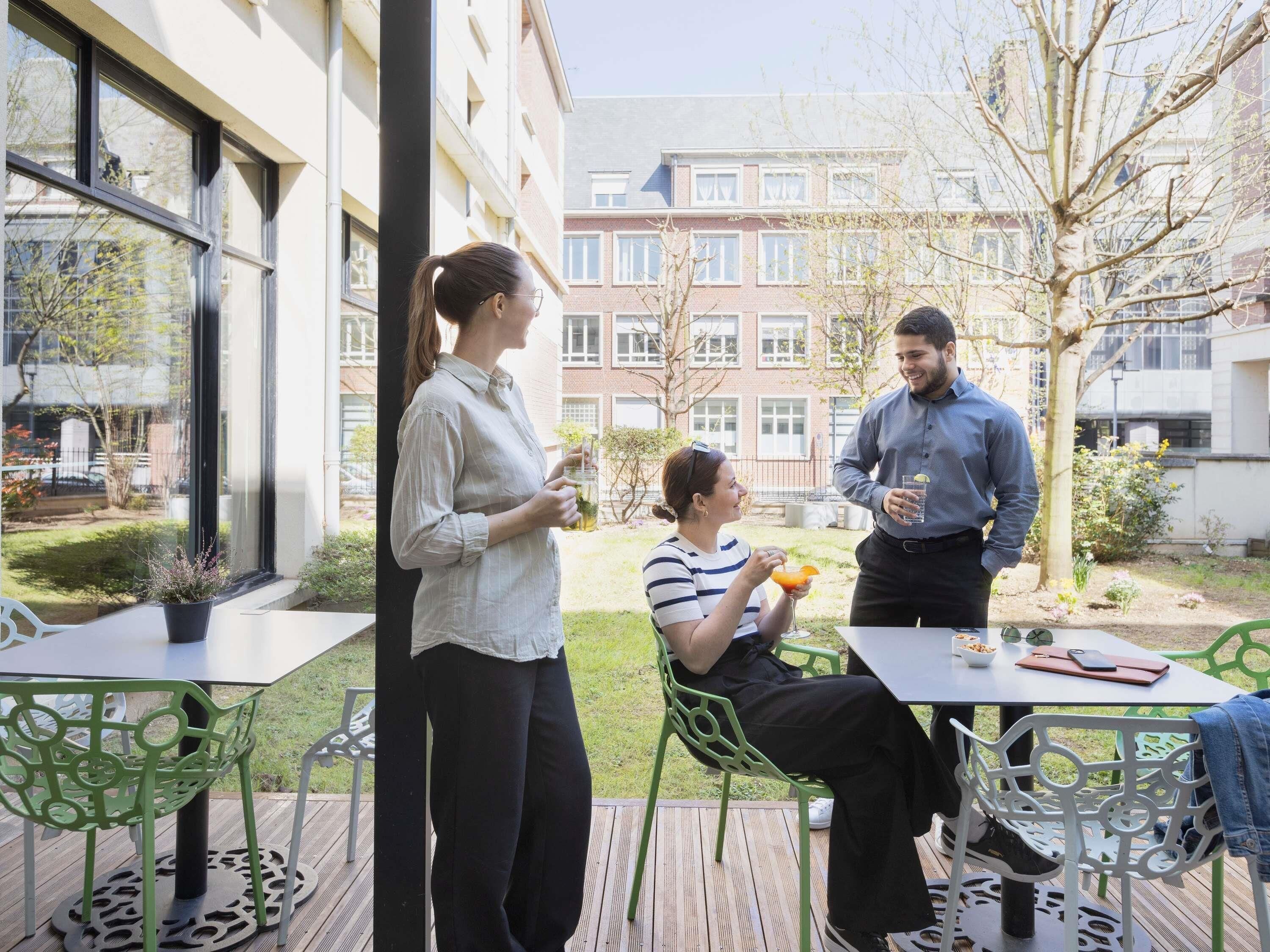 An outdoor patio with tables and chairs, a view of a building, and a garden area.