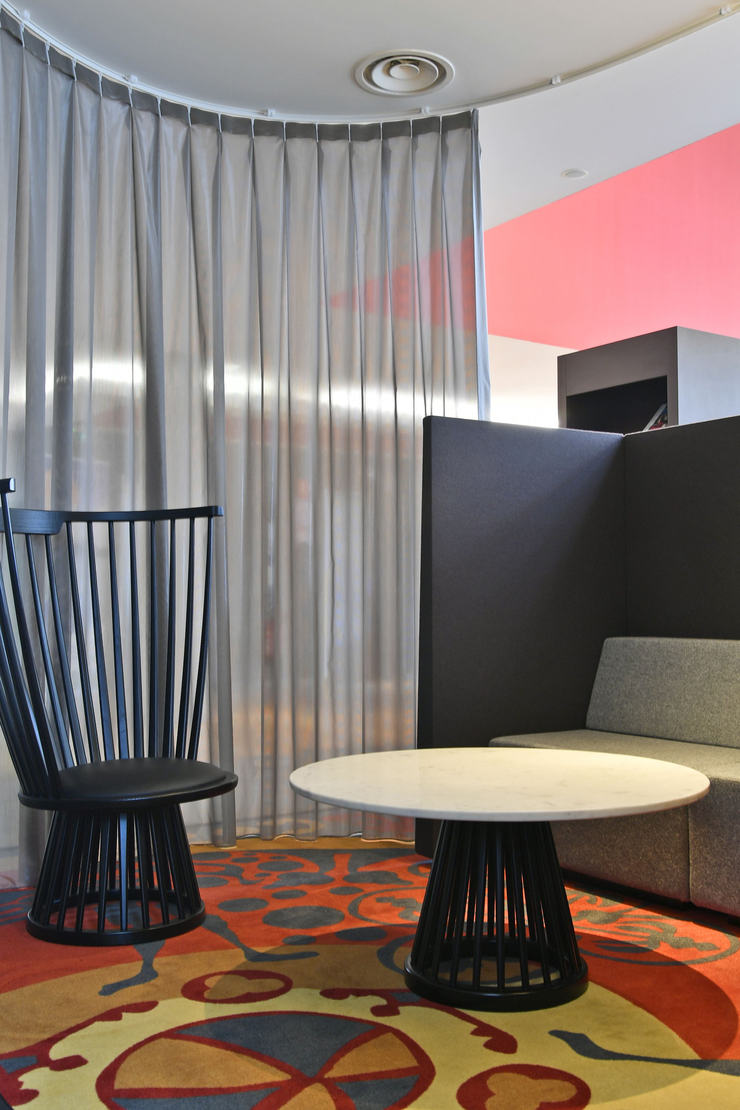 A modern room with a black chair, a round table, a colorful carpet, and a grey sofa.