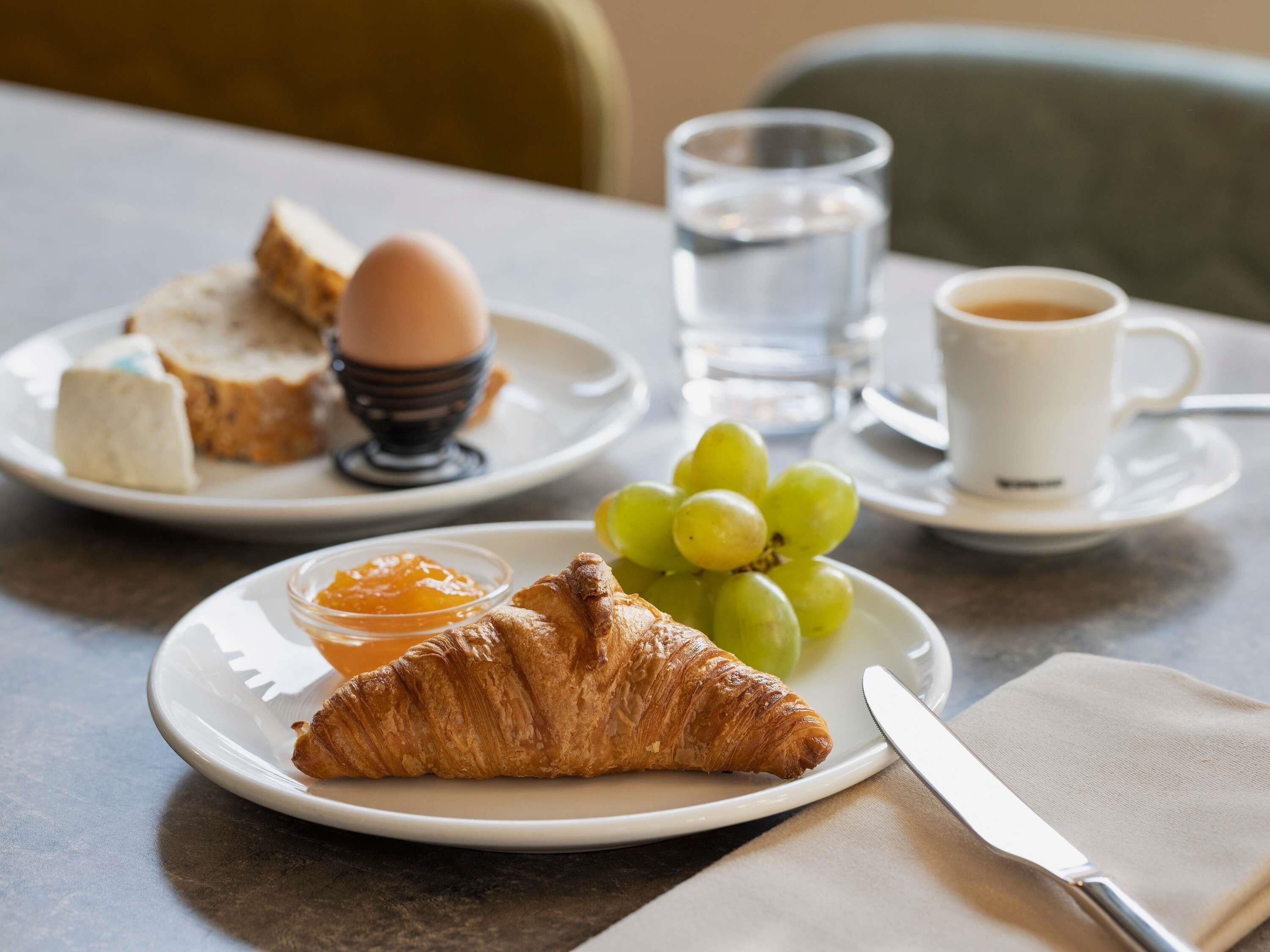 A breakfast setting with croissants, eggs, toast, grapes, and a cup of coffee on a table.