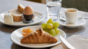 A breakfast setting with croissants, eggs, toast, grapes, and a cup of coffee on a table.