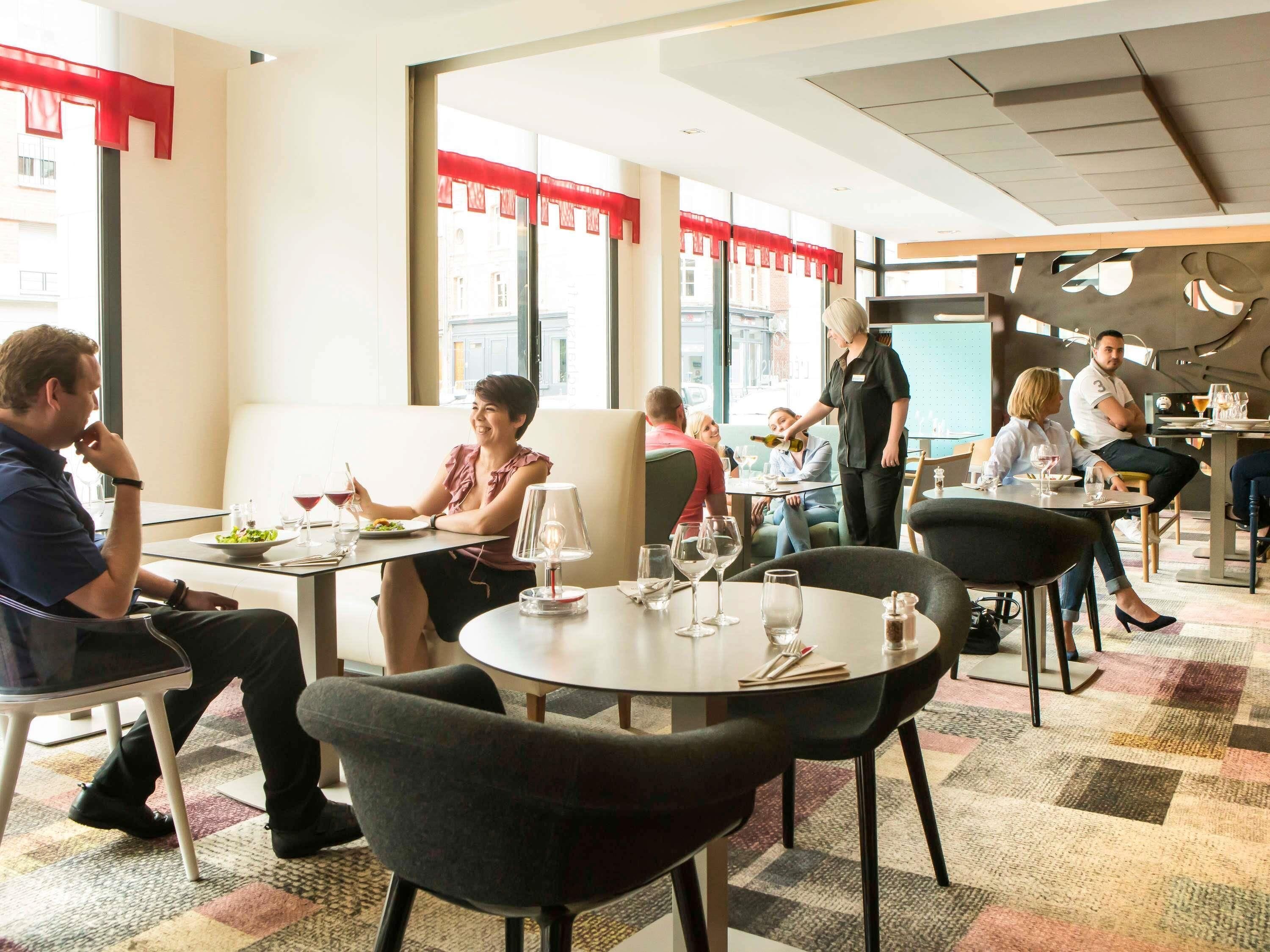 Un espace repas moderne avec des tables rondes, des chaises noires et une vue sur la ville grâce à de grandes fenêtres.