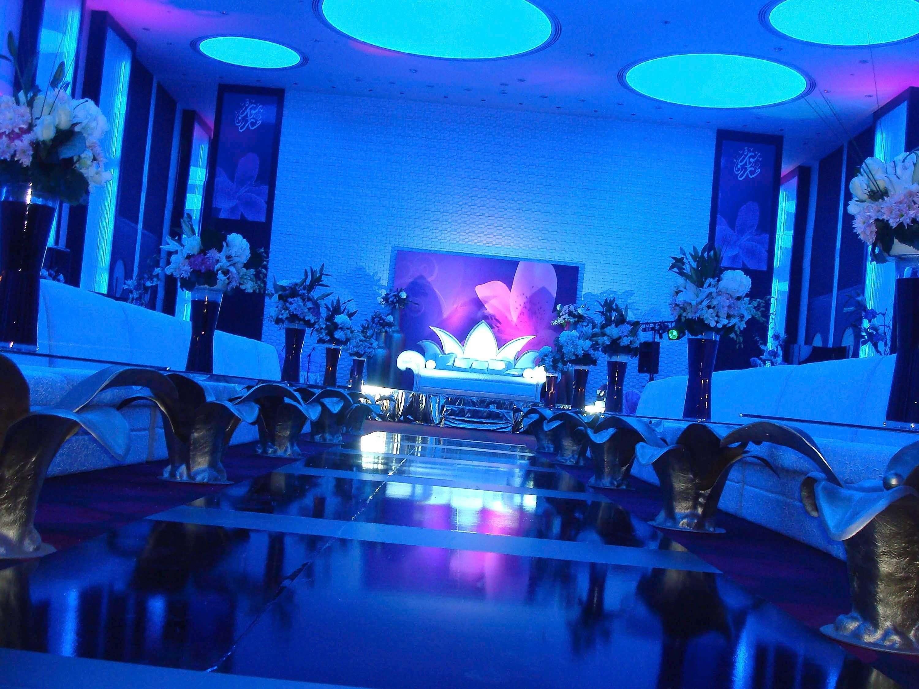 Un salón de conferencias con una larga mesa, sillas y un escenario con un fondo floral.