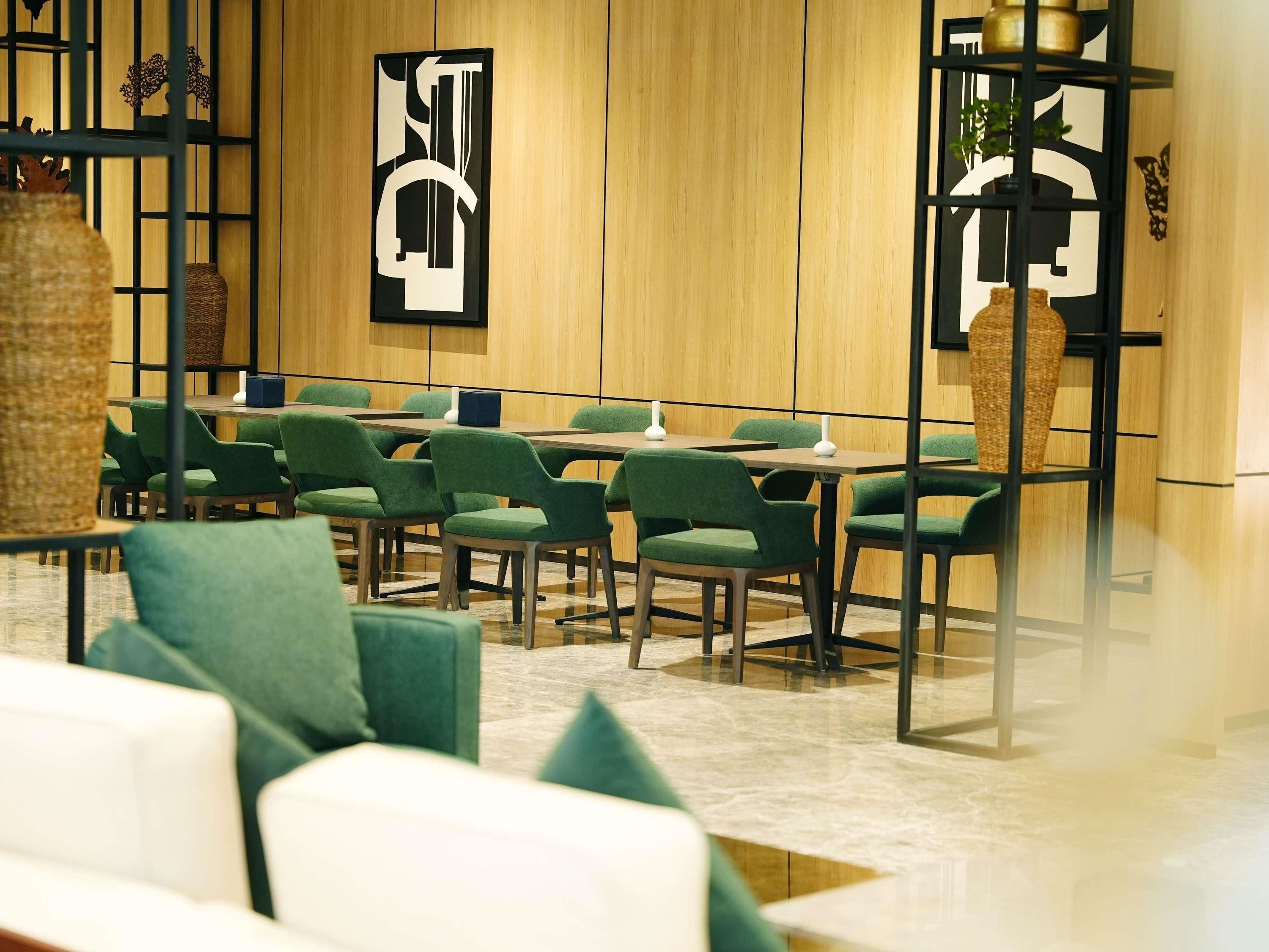 A modern dining area with green upholstered chairs, wooden tables, and decorative wall art.