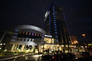 A Novotel hotel with a modern design, featuring a prominent curved facade and illuminated signage.