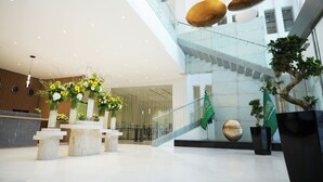 Een moderne lobby met een receptiebalie, een trap en decoratieve planten.