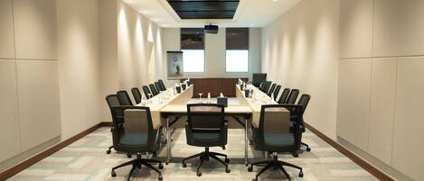 Un salón de conferencias con una larga mesa, varias sillas y una pantalla de proyector.