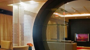 Een moderne hotelkamer met een glazen scheidingswand, een flatscreen televisie, een bank en een bijzettafeltje.