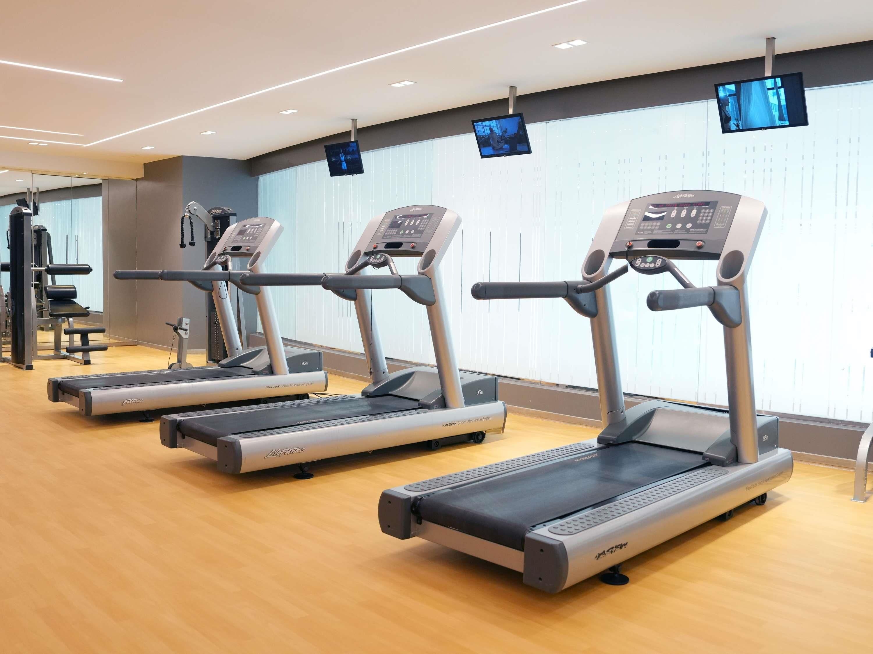 Three treadmills, a weight bench, and a wall-mounted TV in a gym.