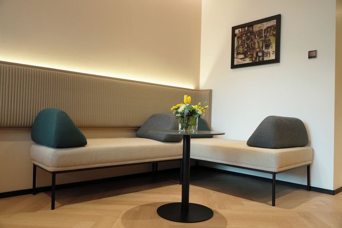 A modern seating area with a sofa and a small table, a vase with flowers, and a framed artwork on the wall.