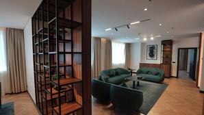 A modern living room with a sectional sofa, a coffee table, and a wooden bookshelf. - Novotel Riyadh Al Anoud (Riyadh)
