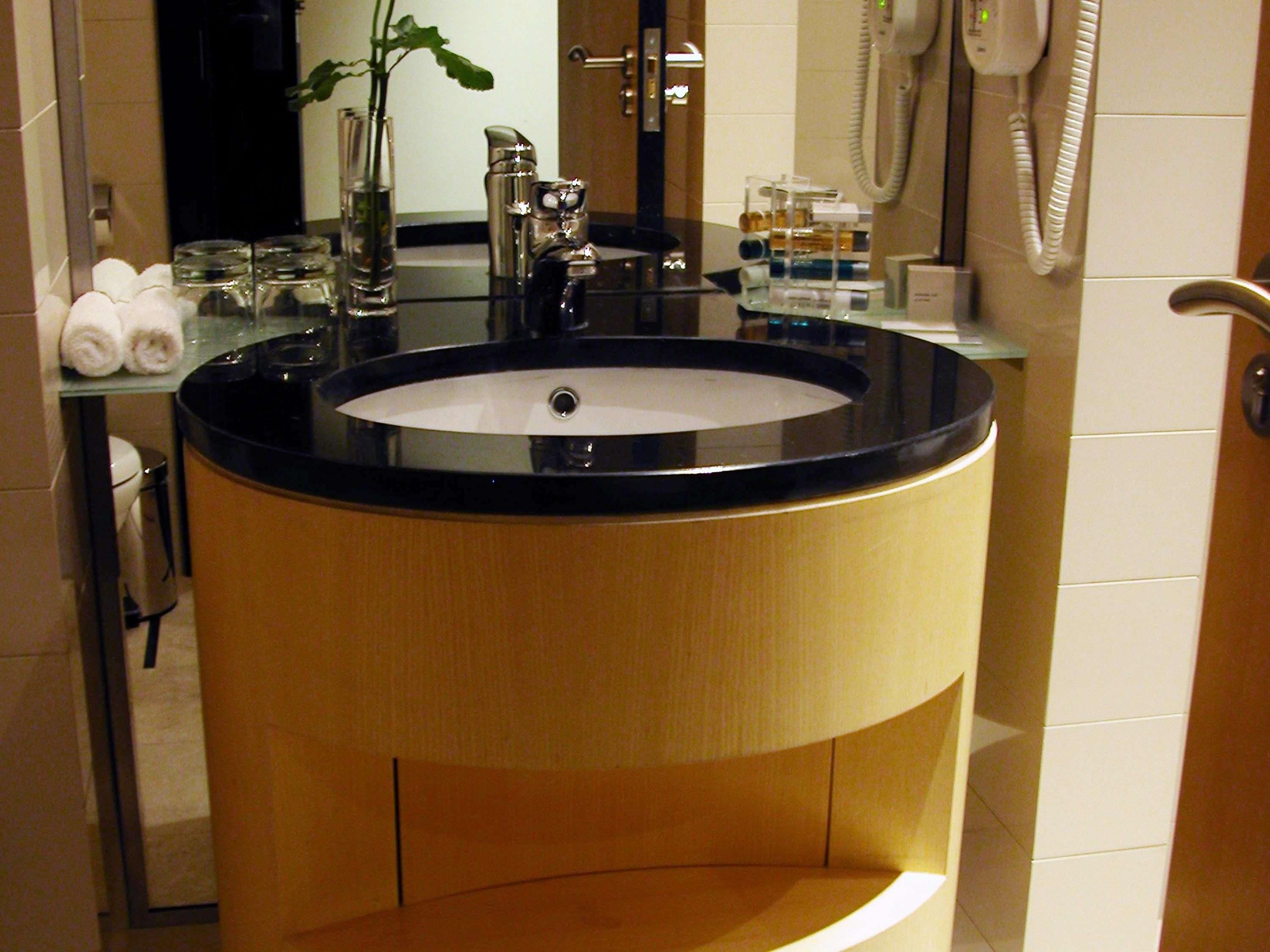 Un baño con un lavabo redondo, un espejo, un toallero y un teléfono.