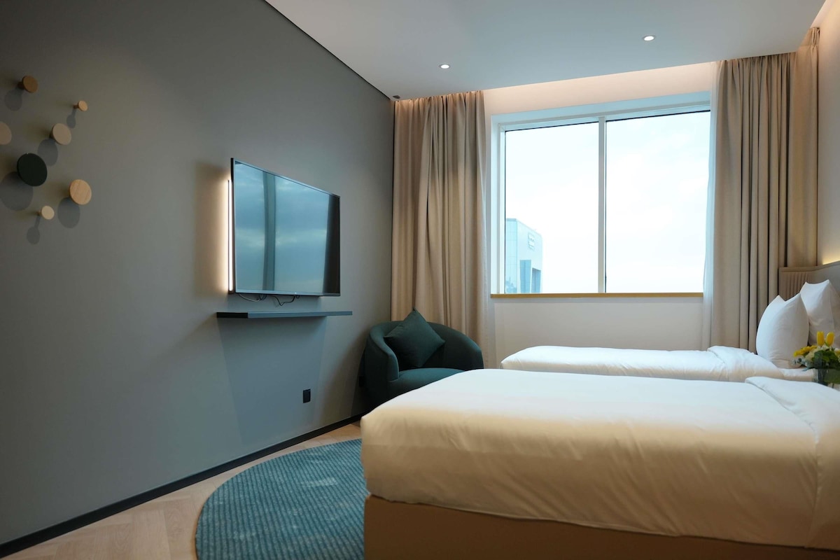 A hotel room with a TV, two beds, a window with curtains, and a patterned rug.