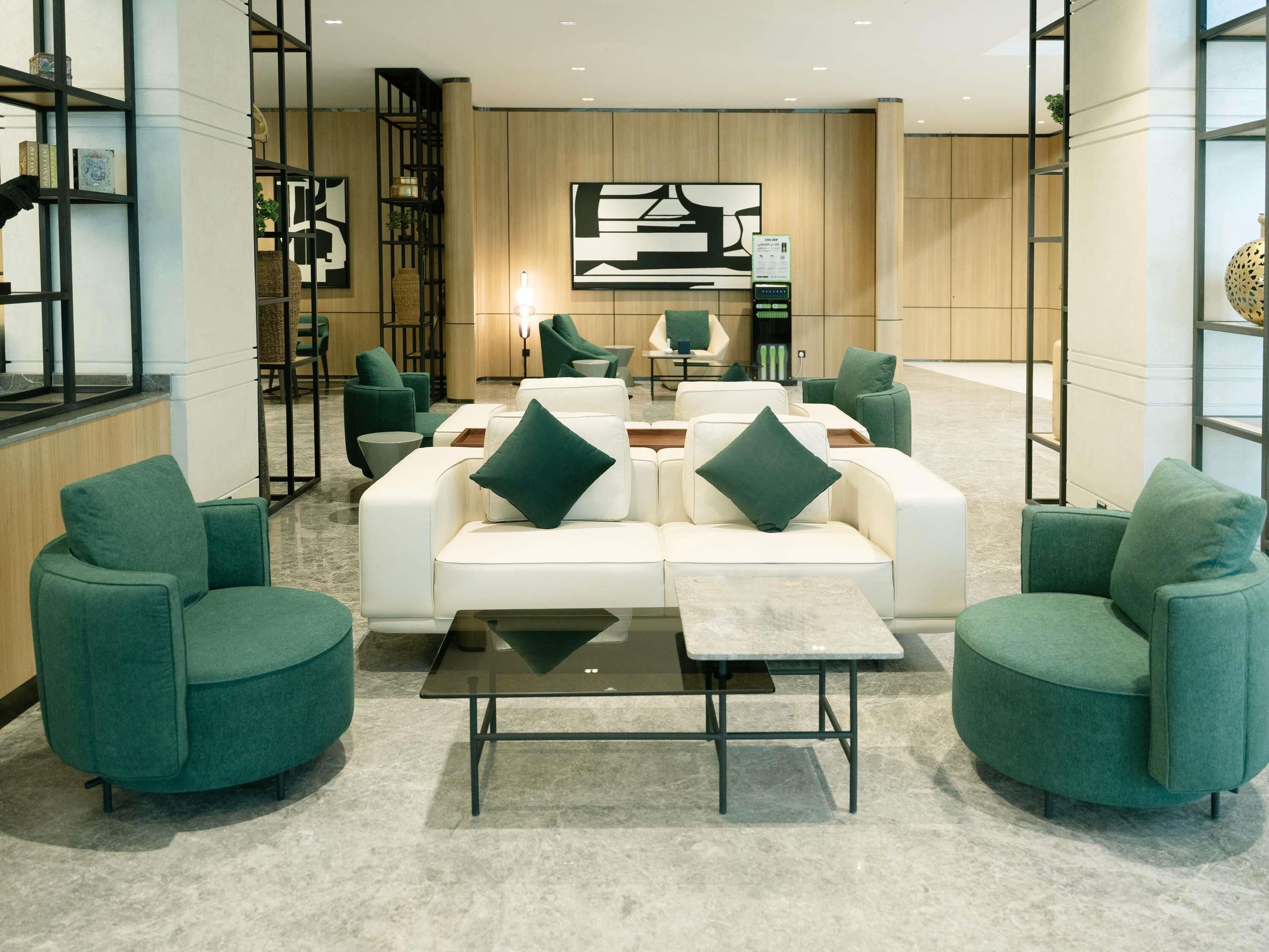 Eine moderne Lobby mit einer Sitzecke, ausgestattet mit einem weißen Sofagarnitur, grünen Sesseln und einem Couchtisch.
