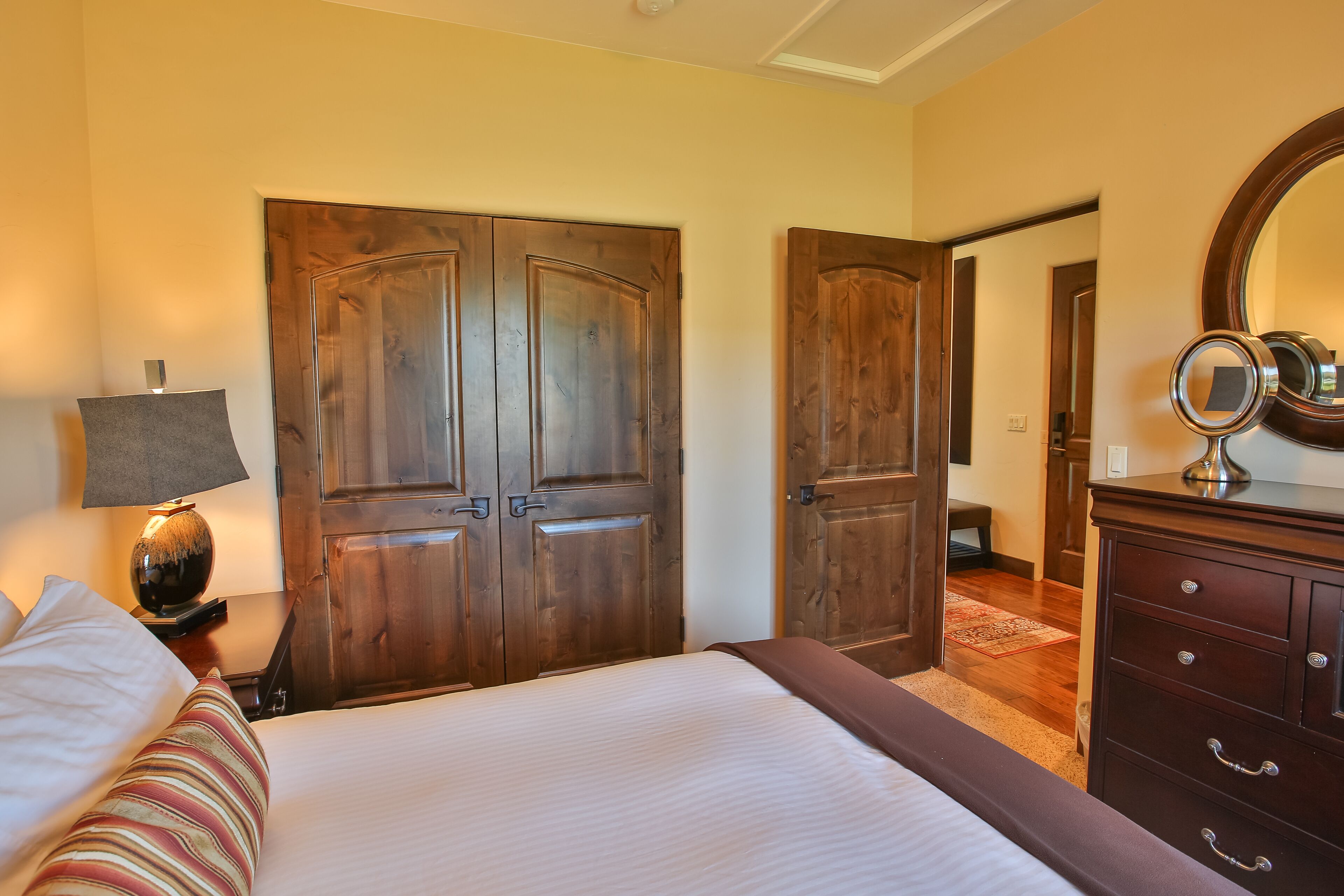 Un dormitorio con cama, cómoda, espejo y puertas de madera.