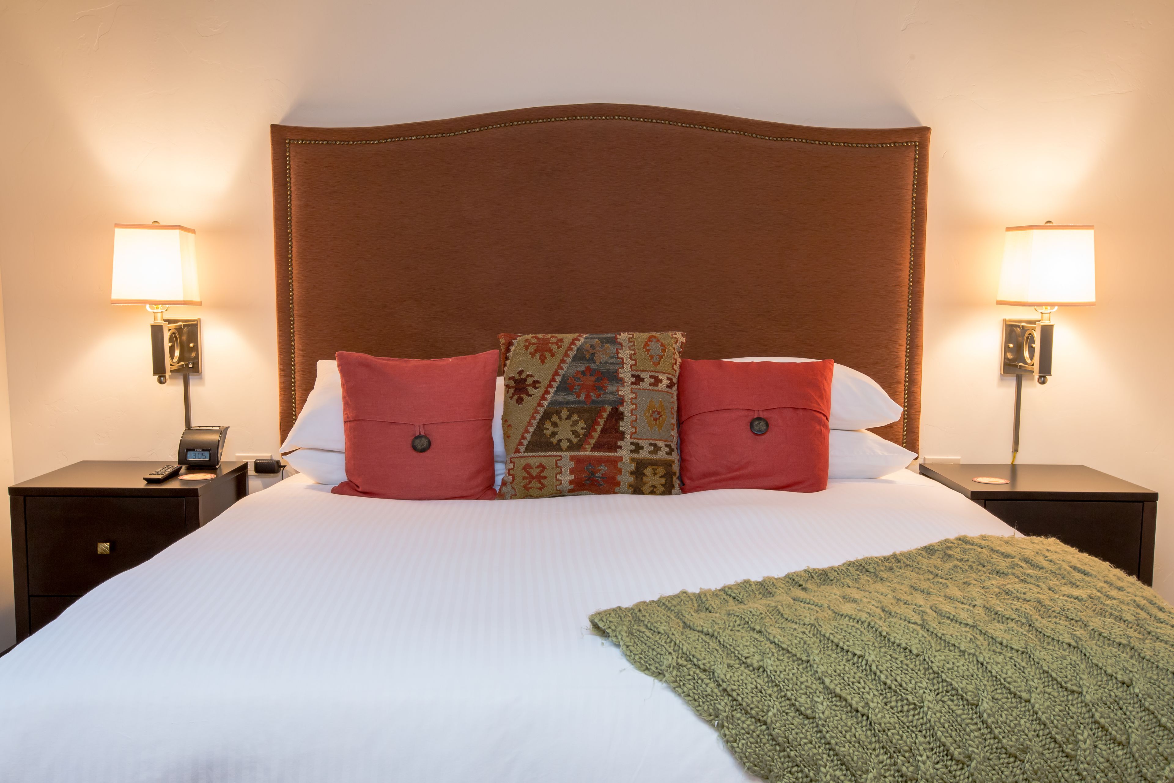 A neatly made bed with a brown headboard, two bedside lamps, and a patterned throw blanket.