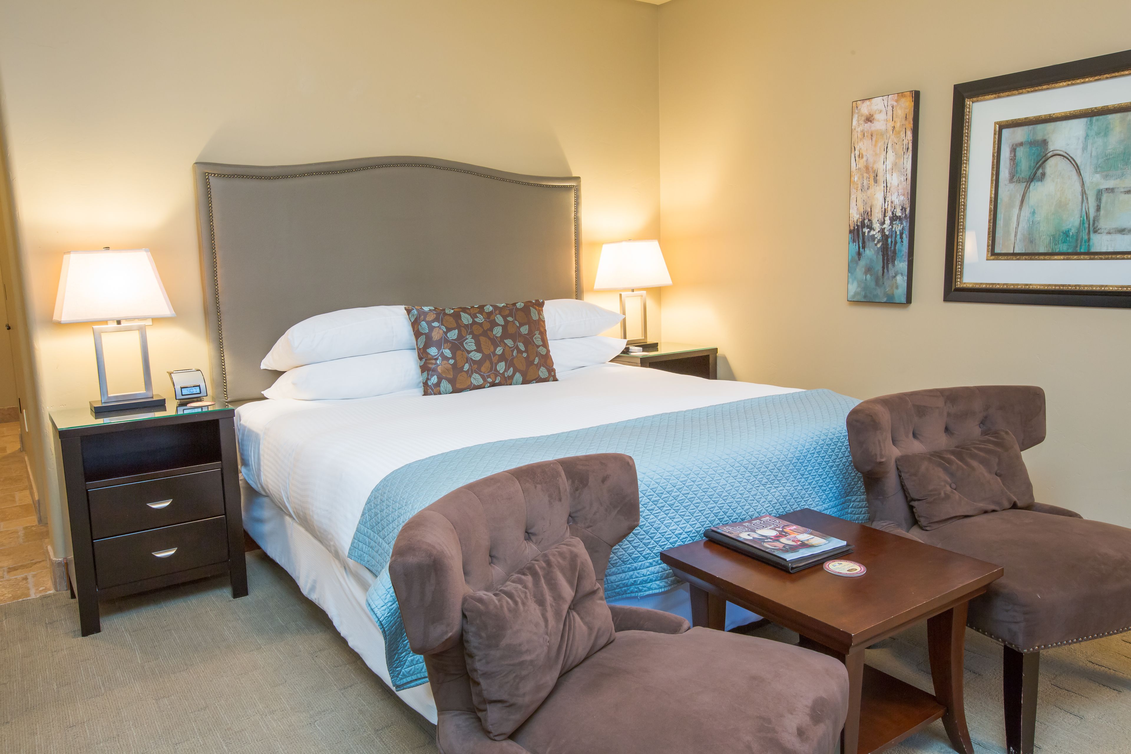 A hotel room with a large bed, two bedside tables with lamps, a small table with a book, and two armchairs.