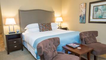 A hotel room with a large bed, two bedside tables with lamps, a small table with a book, and two armchairs.