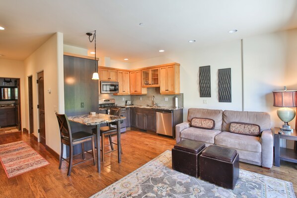 A modern kitchen with wooden cabinets, a dining area with a table and chairs, a sofa, and a lamp. - Columbia Cliff Villas Hotel (Hood River)