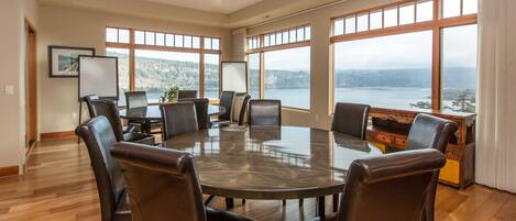 A conference room with a large table surrounded by chairs, large windows with a view of a lake and mountains, and a whiteboard on the left wall.