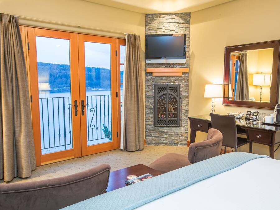Quarto de hotel com cama, escrivaninha, televisão, lareira e varanda com cortinas.