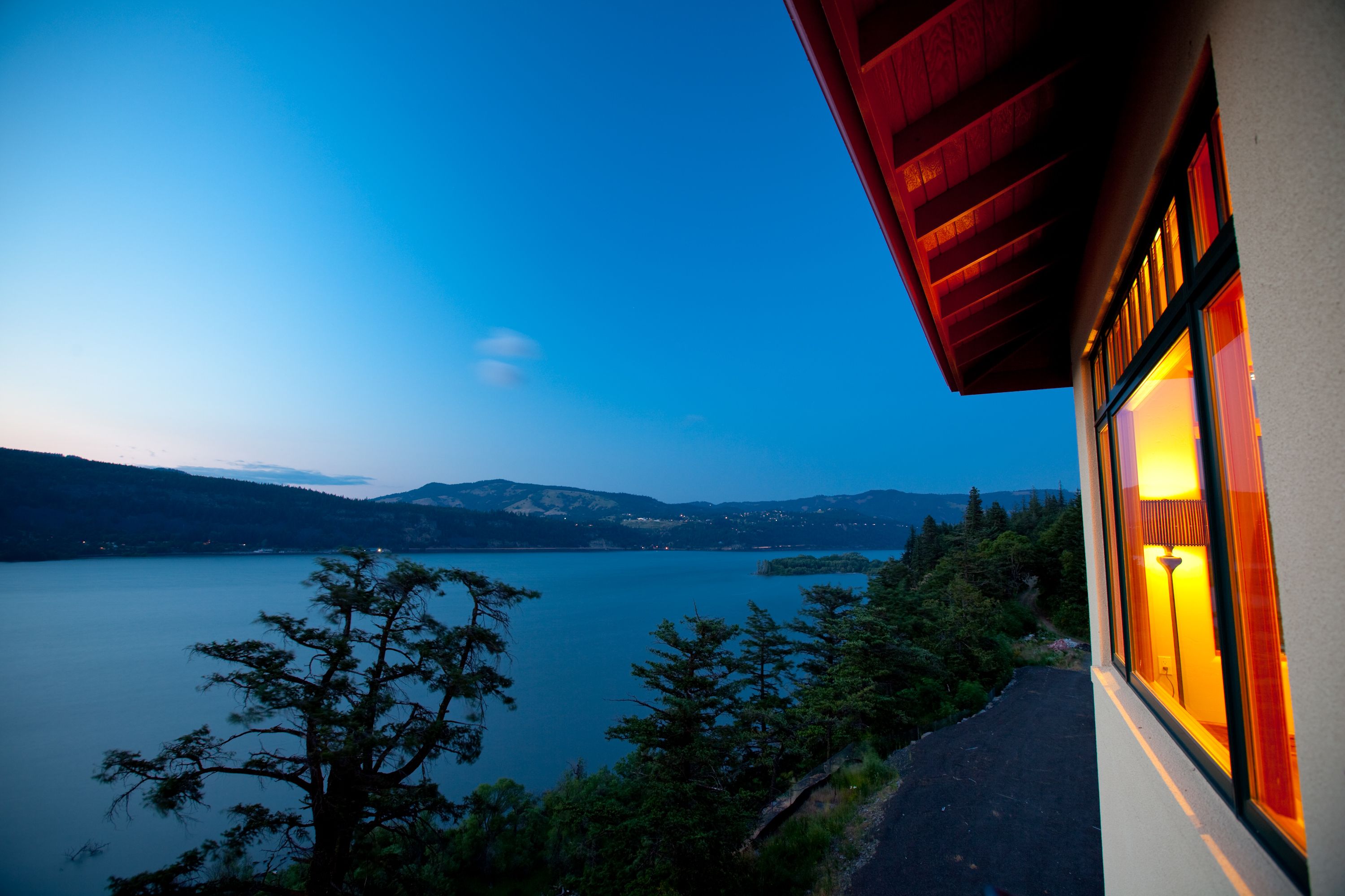 A lakeside view from a building with a red roof and a window with warm lighting.