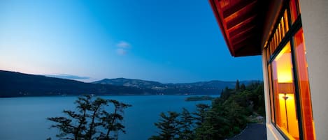 A lakeside view from a building with a red roof and a window with warm lighting.