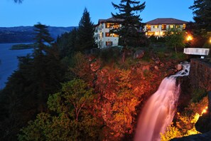 A multi-story house with a waterfall in front, surrounded by trees and a lake. - Columbia Cliff Villas Hotel (Hood River)
