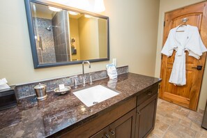 A bathroom with a marble countertop, a sink, a mirror, and a wooden door with a towel hanging on it. - Columbia Cliff Villas Hotel (Hood River)