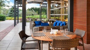 Een terras met rieten meubels, een houten tafel en een glazen scheidingswand.