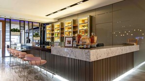 Een moderne barruimte met een marmeren aanrecht, meerdere planken met flessen, en een zithoek met barstoelen.