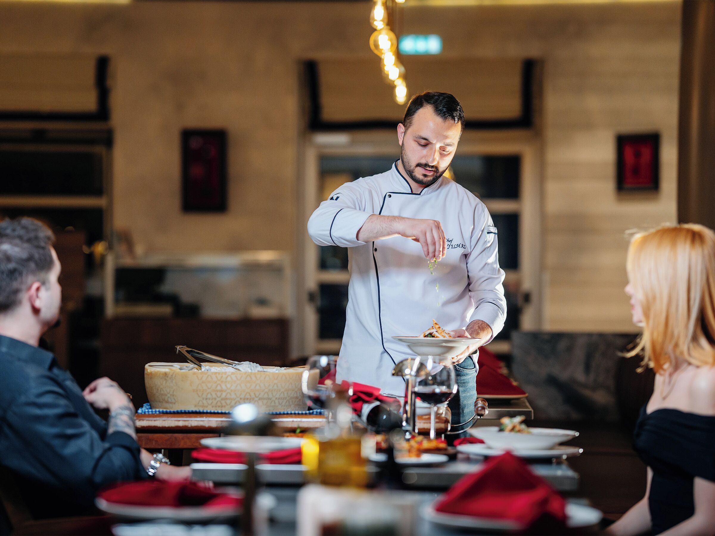 A chef preparing food in a restaurant setting with tables and chairs.
