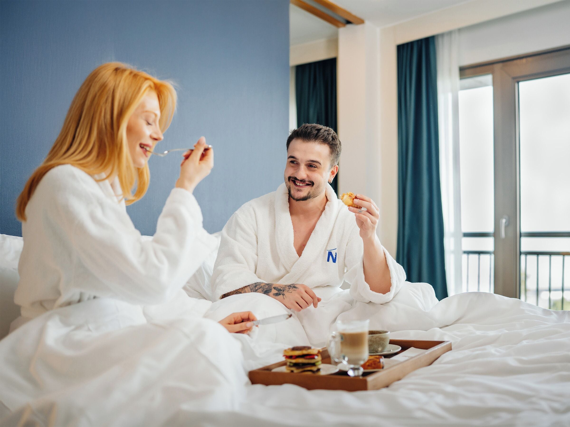 Una habitación de hotel con cama, una bandeja con alimentos para el desayuno y una ventana con cortinas.