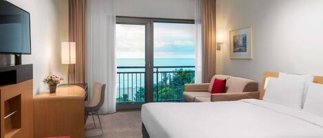 A hotel room with a bed, a desk, a chair, a TV, and a balcony with a view.