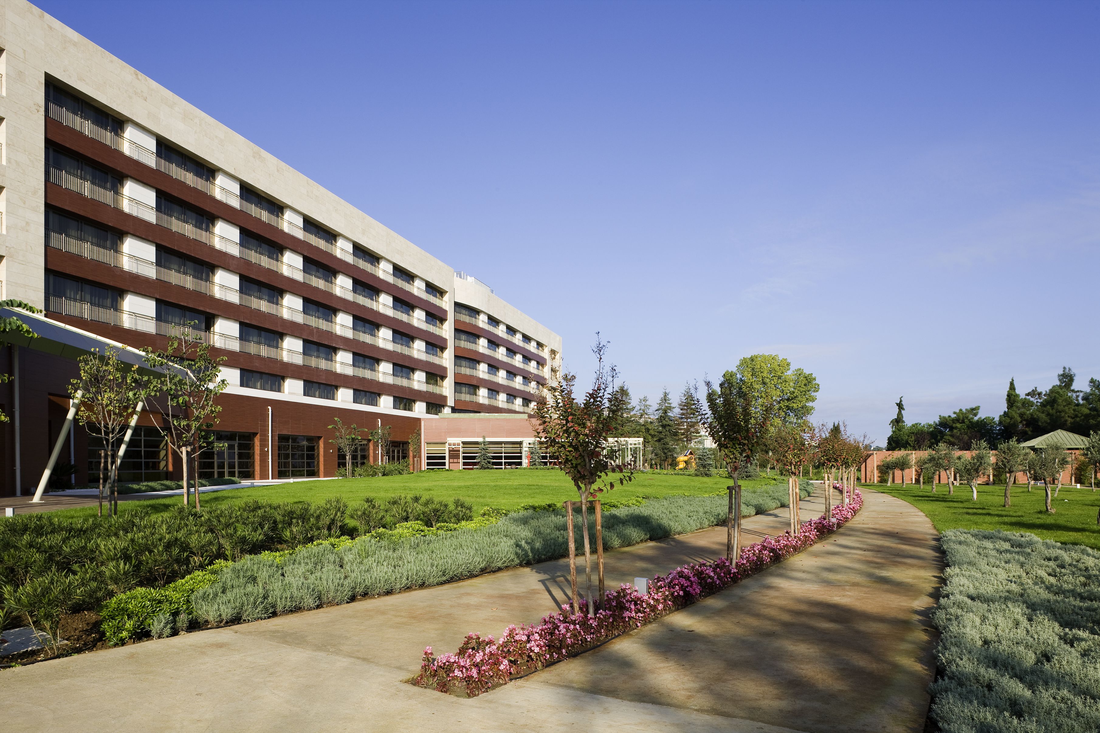 A modern building with a long, straight pathway lined with neatly trimmed hedges and small trees.