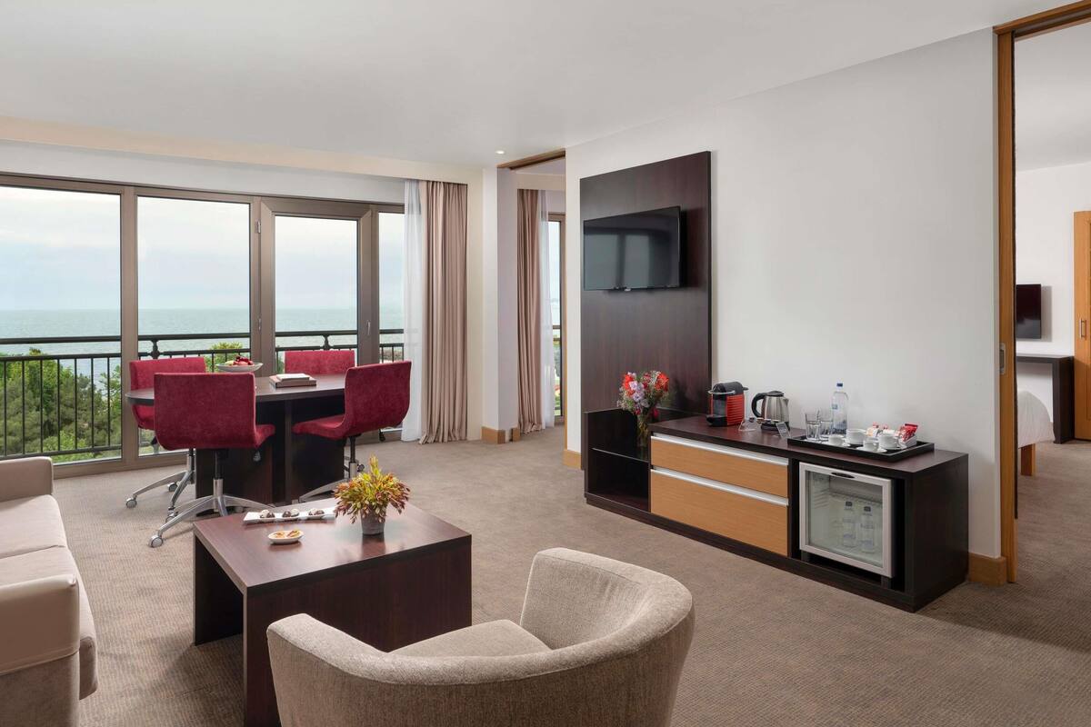 A hotel room with a balcony, a dining area, a TV, and a minibar.