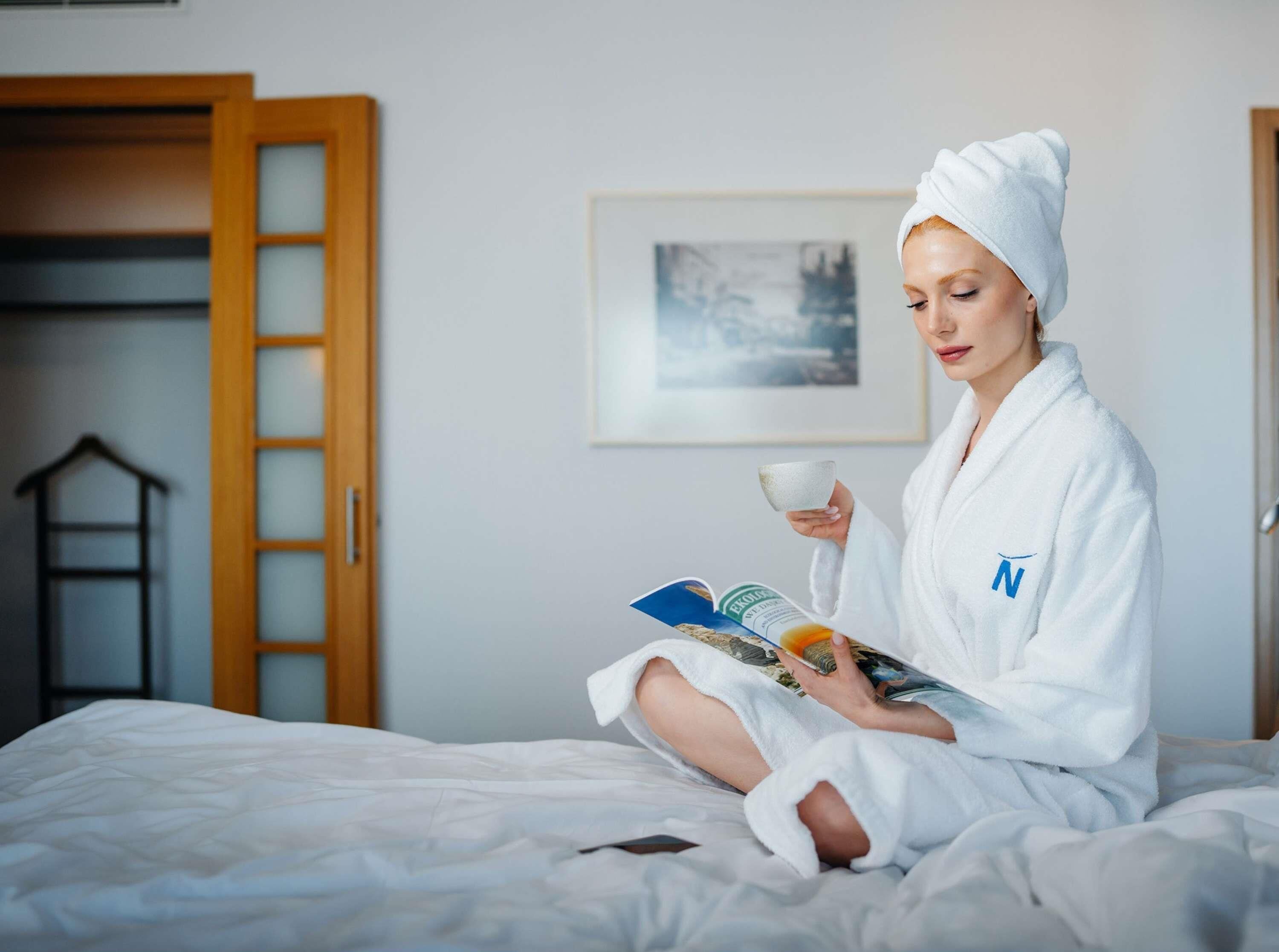 Una persona seduta su un letto in una stanza con una porta di legno, un quadro appeso al muro e un armadio.
