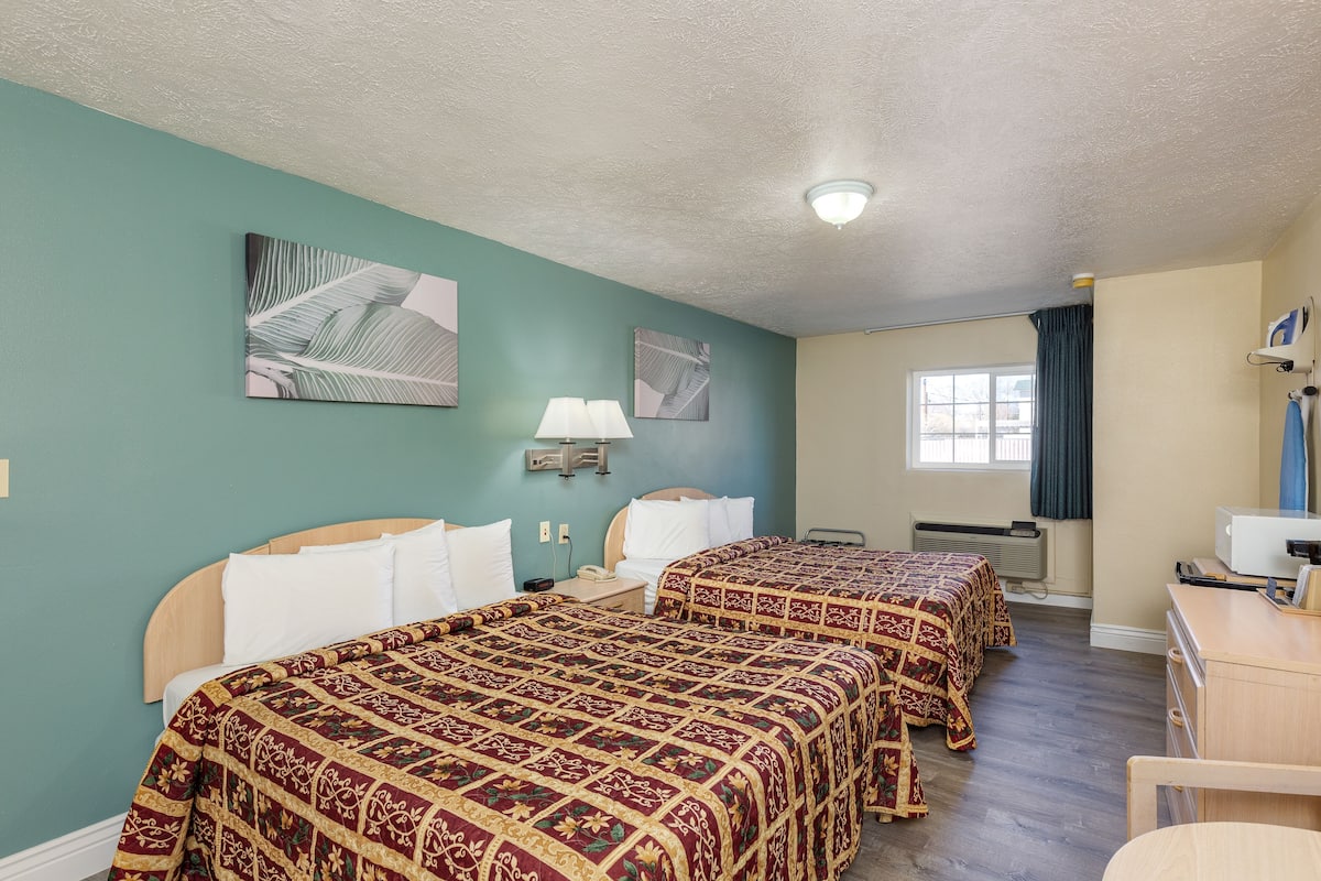 A hotel room with two beds, a desk, a chair, a window with curtains, and wall-mounted artwork.