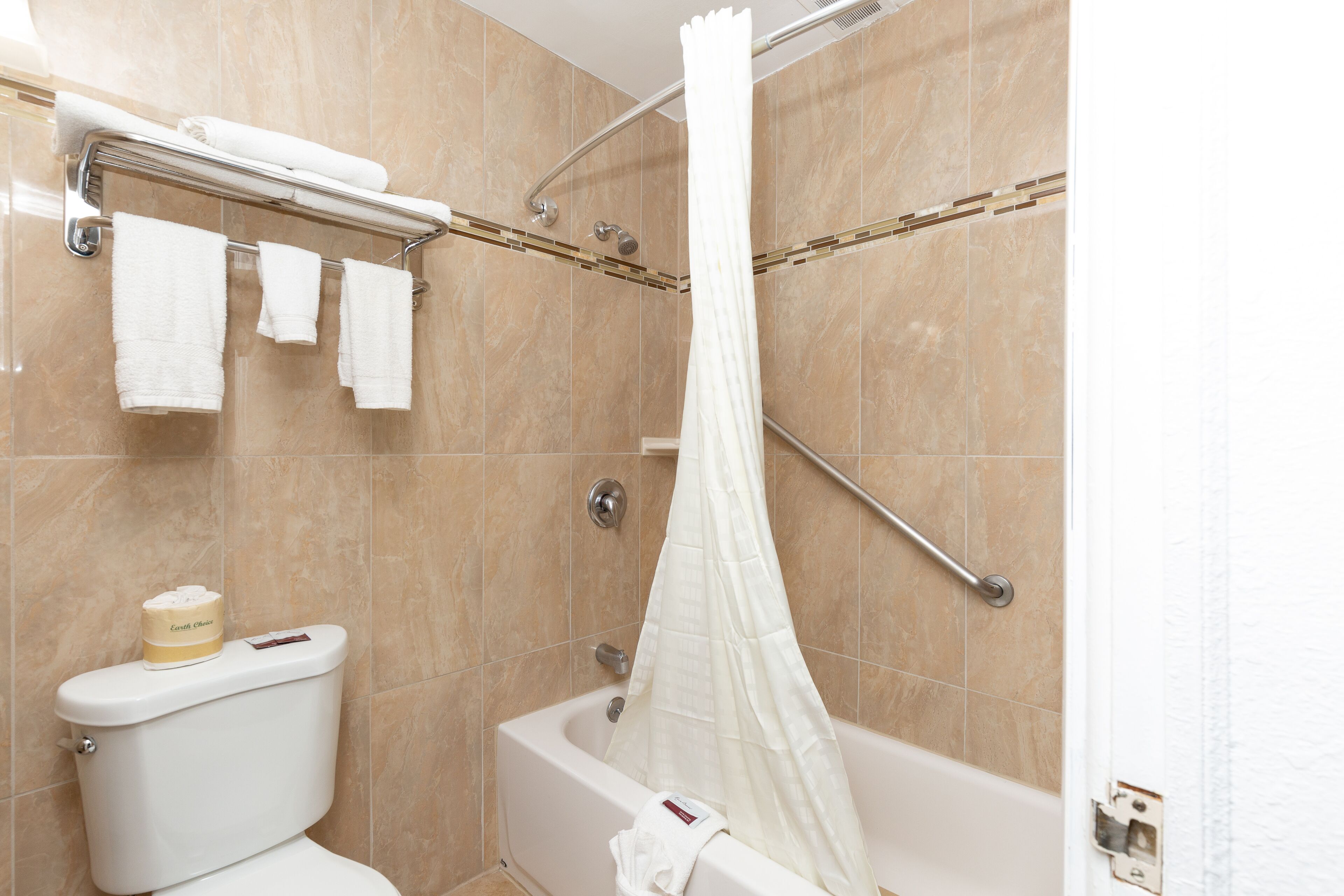 Un bagno con una vasca, una doccia con tenda bianca e un water con dispenser di sapone.