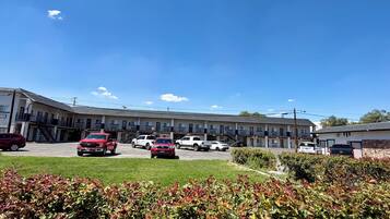 A motel with multiple parking spaces, a staircase leading to the entrance, and a clear blue sky.
