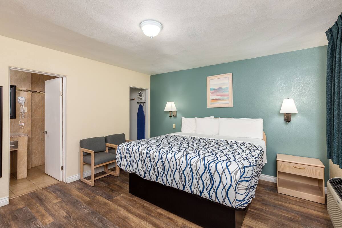 A bedroom with a bed, bedside lamps, a nightstand, a chair, and a door leading to a bathroom.
