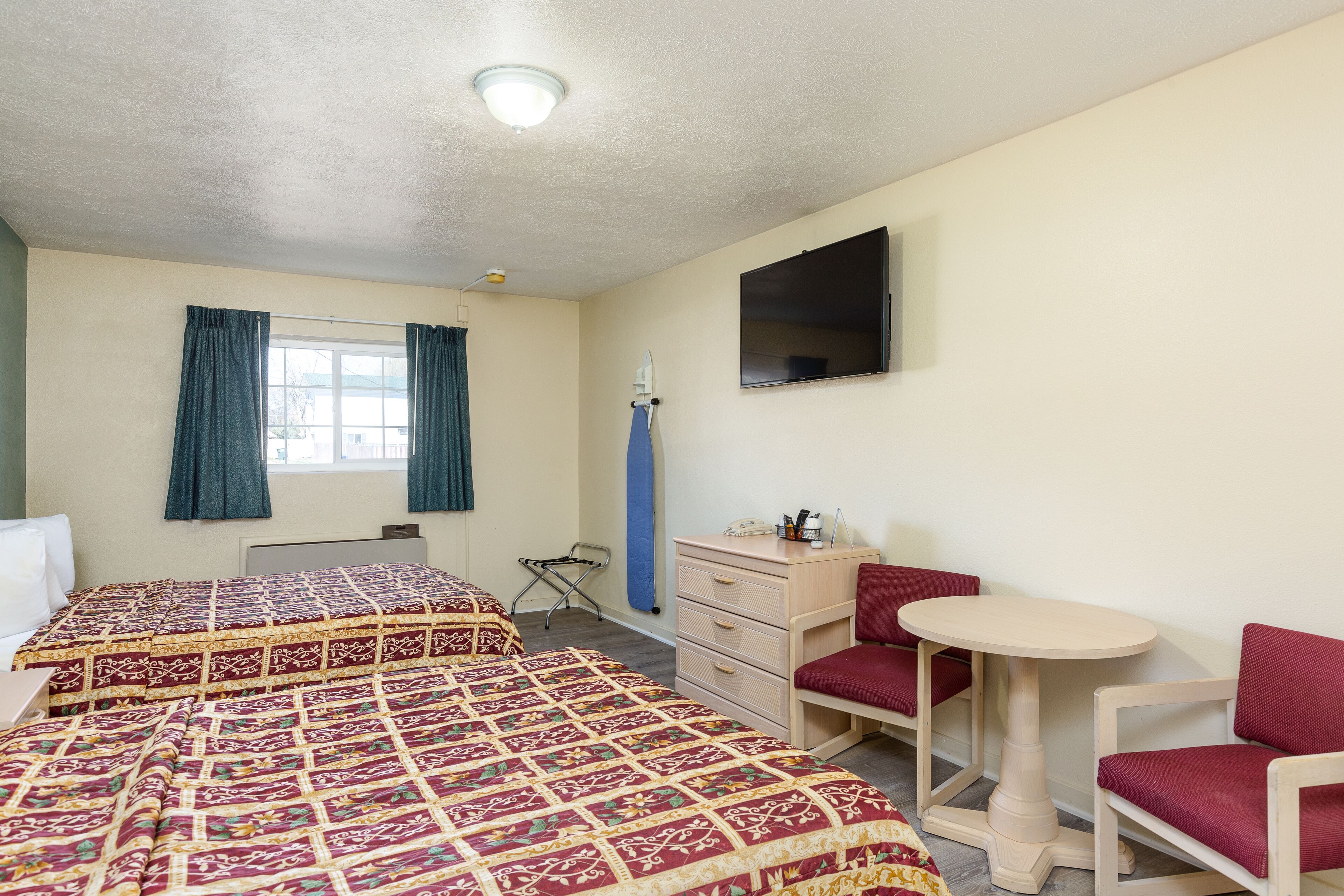 A room with two beds, a desk, a chair, a small table, and a TV on the wall.
