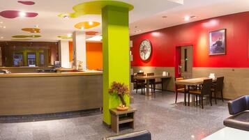 A modern hotel lobby with a reception desk, seating area, and a large wall clock.