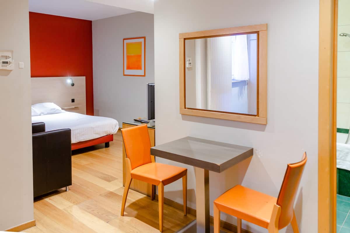 A hotel room with a bed, a desk with a chair, a television, and a mirror on the wall.