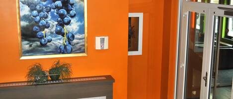 An interior with orange walls, a reception desk with a plant, and a glass door leading to another room.