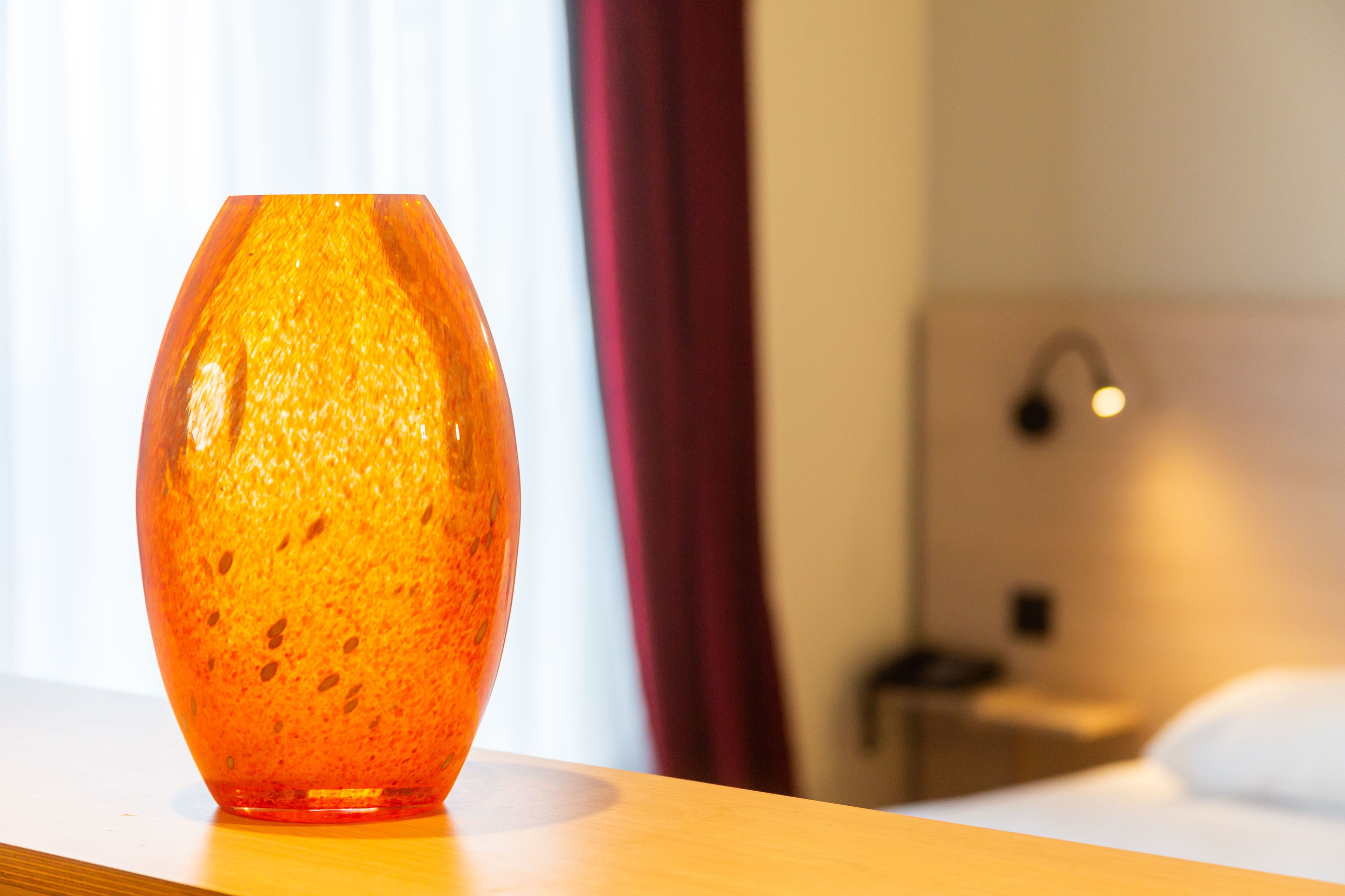 Ein Hotelzimmer mit Nachttisch aus Holz, einer Lampe und einem Bett mit weißer Bettwäsche.