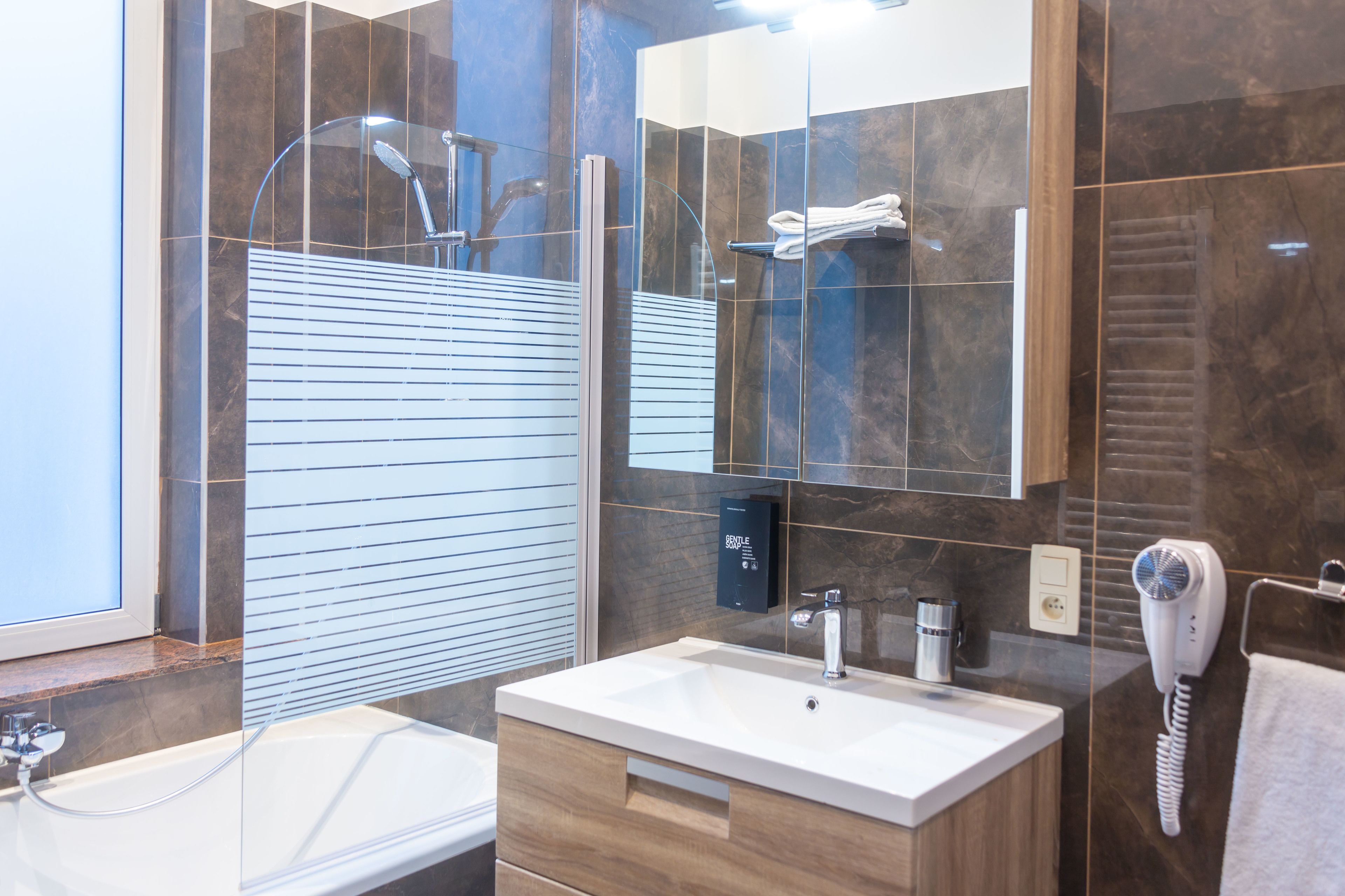 Un baño moderno con ducha envuelta en vidrio, un lavamanos blanco y un secador de pelo en la pared.