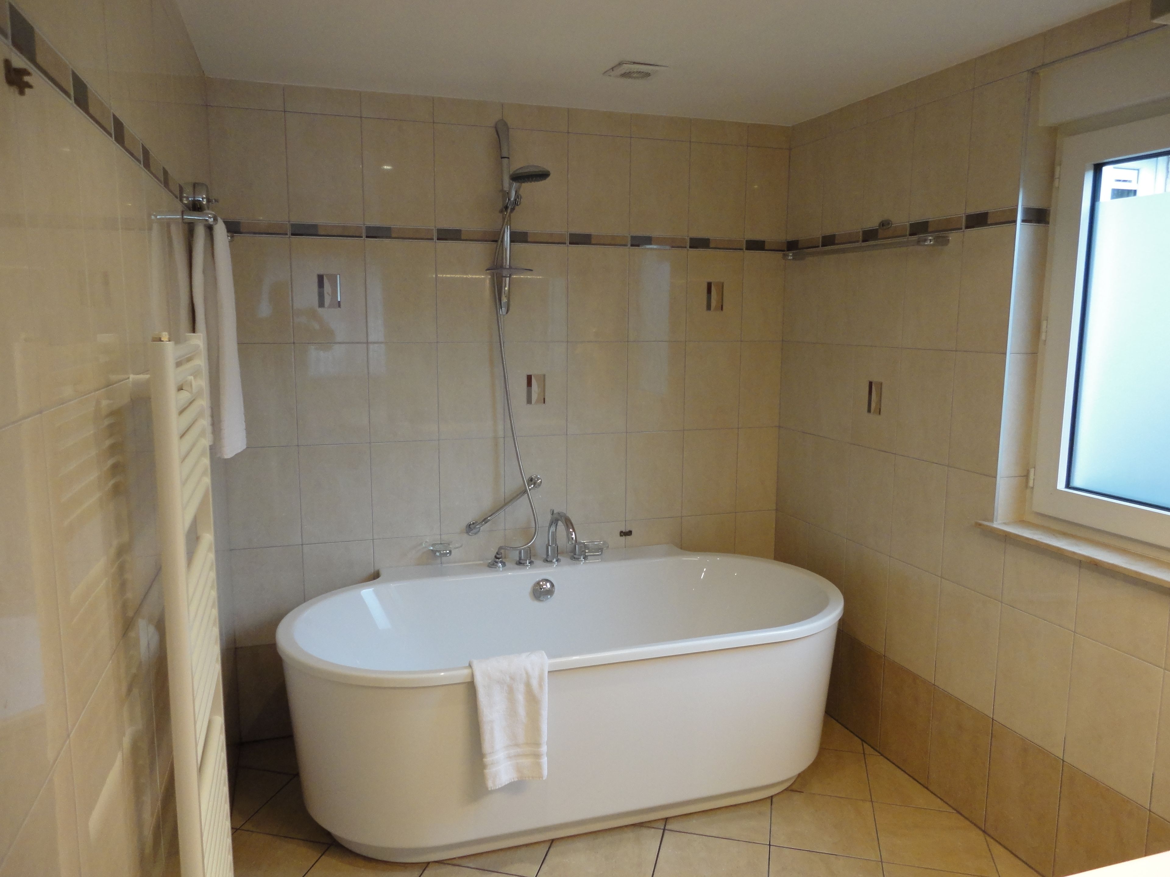 A bathroom with a freestanding bathtub, a showerhead, and a window.