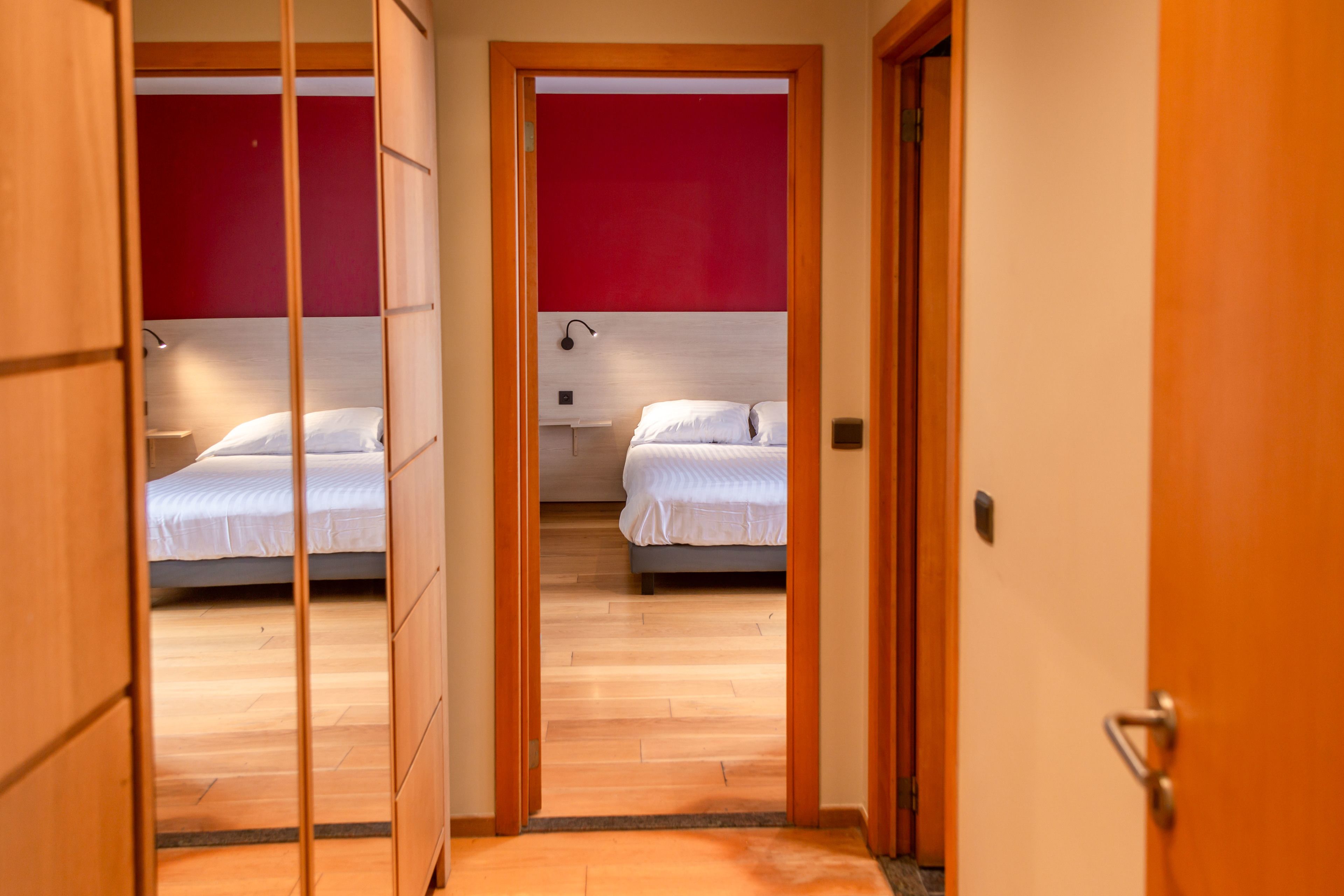 Een gang die leidt naar twee slaapkamers met houten vloeren en rode muren.