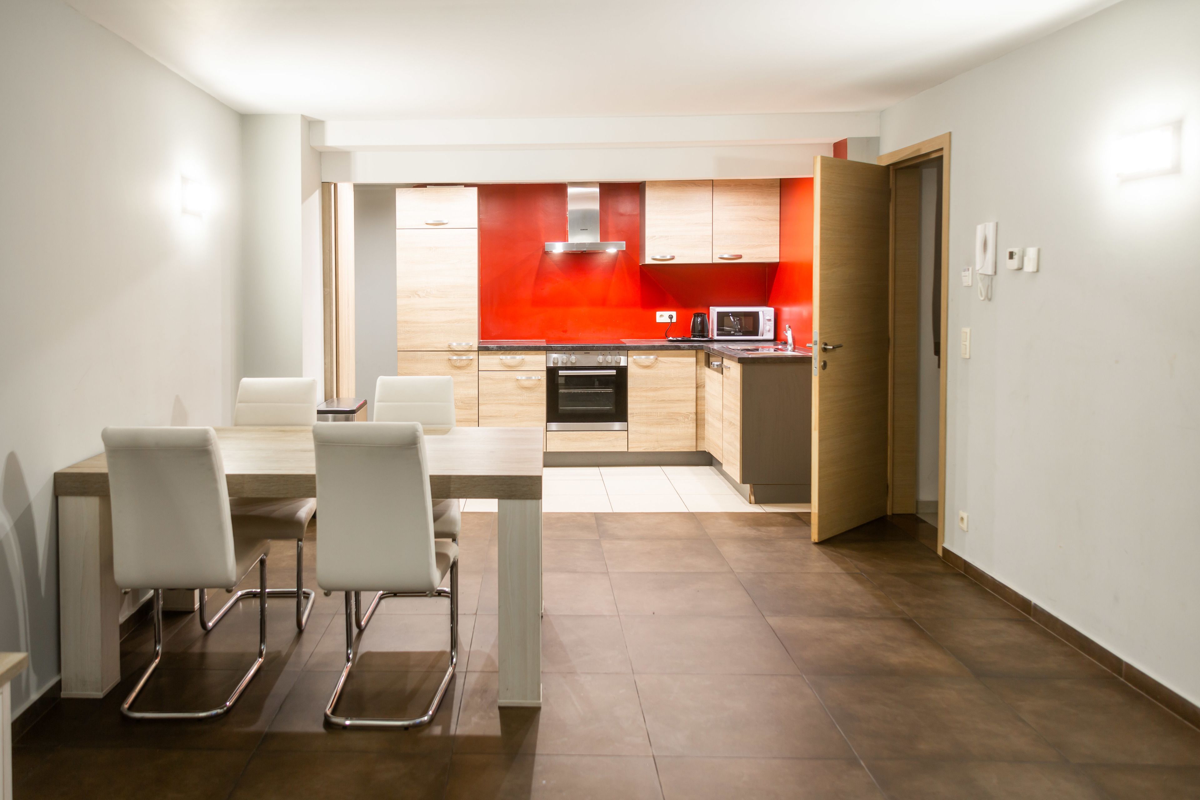 A modern kitchen with wooden cabinets, a microwave, and an oven. There is a dining area with a table and chairs.